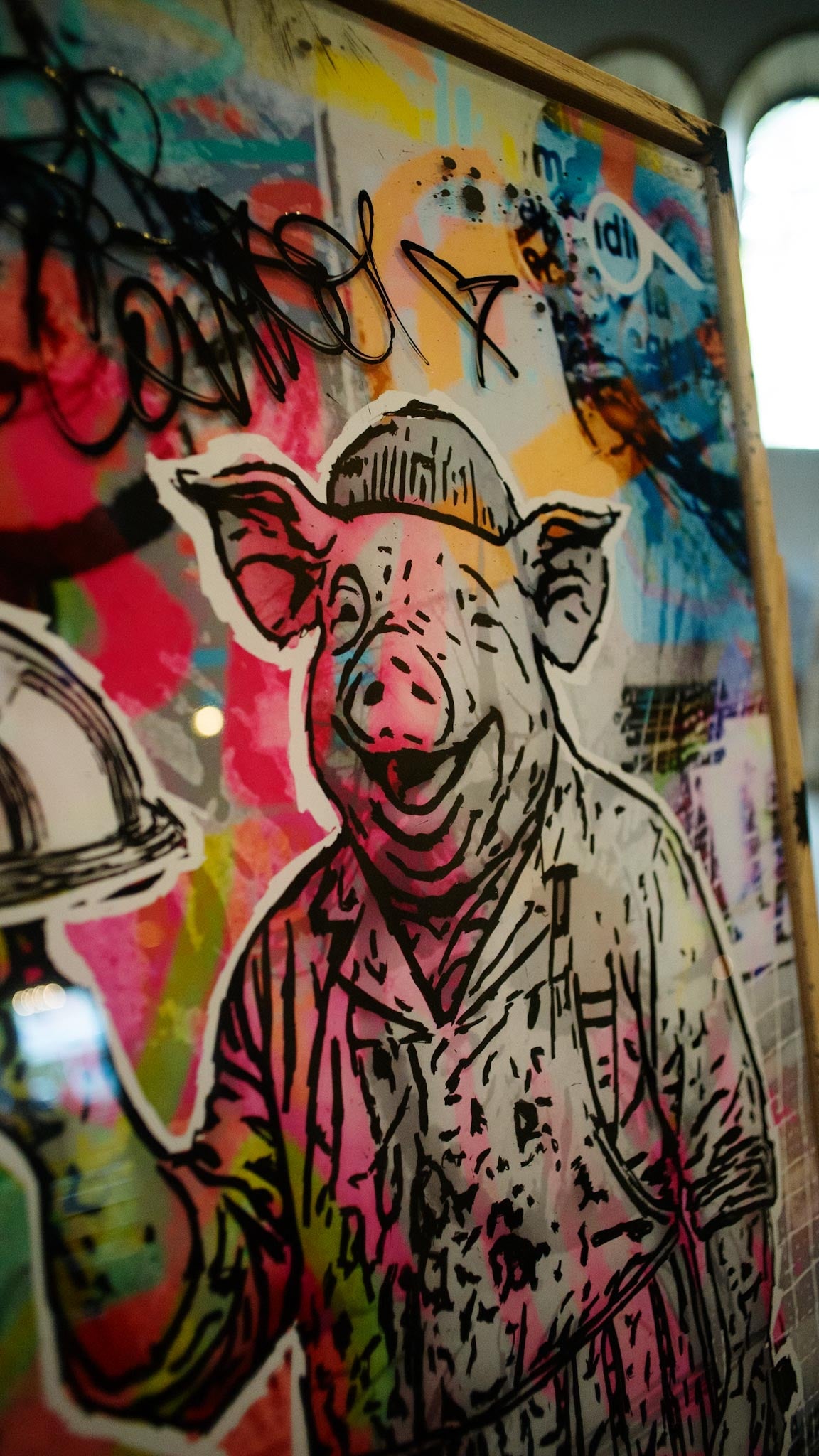 Nahaufnahme Mr. Butcher: lachender Schweinekopf mit Mütze, Tags und knallige Farben auf Acrylglas