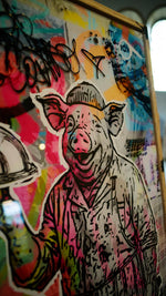 Nahaufnahme Mr. Butcher: lachender Schweinekopf mit Mütze, Tags und knallige Farben auf Acrylglas